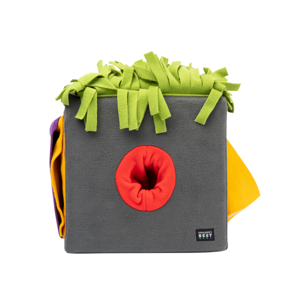 Graue Futterbox mit bunten, fransigen Stoffstreifen in Grün, Orange und Gelb. Die Box hat eine runde Öffnung in der Mitte.