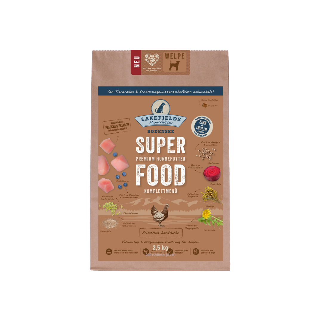Verpackung von Lakefields Superfood für Hunde, 1 kg. Braune Tüte mit Bildern von Landhuhn, Kräutern und dem Text 'NEU' und 'WELPE'.