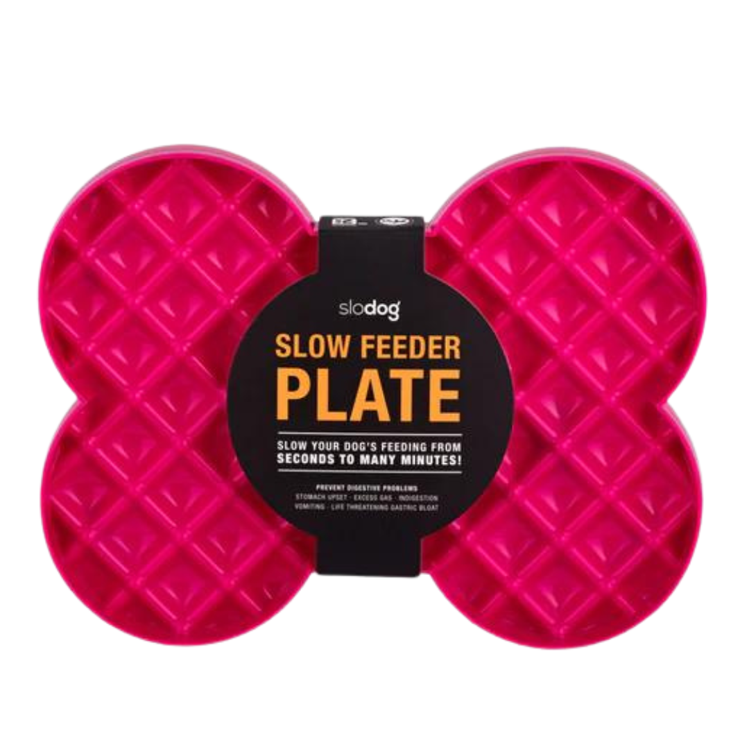 Pinke Futterplatte 'LickiMat Slodog' in Form eines Knochens mit rautenförmigen Vertiefungen. Verpackung zeigt einen Hund und Informationen zur Verwendung.