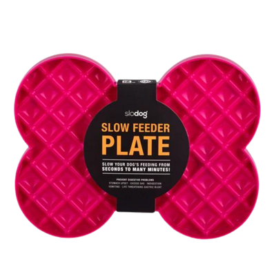 Pinke Futterplatte 'LickiMat Slodog' in Form eines Knochens mit rautenförmigen Vertiefungen. Verpackung zeigt einen Hund und Informationen zur Verwendung.