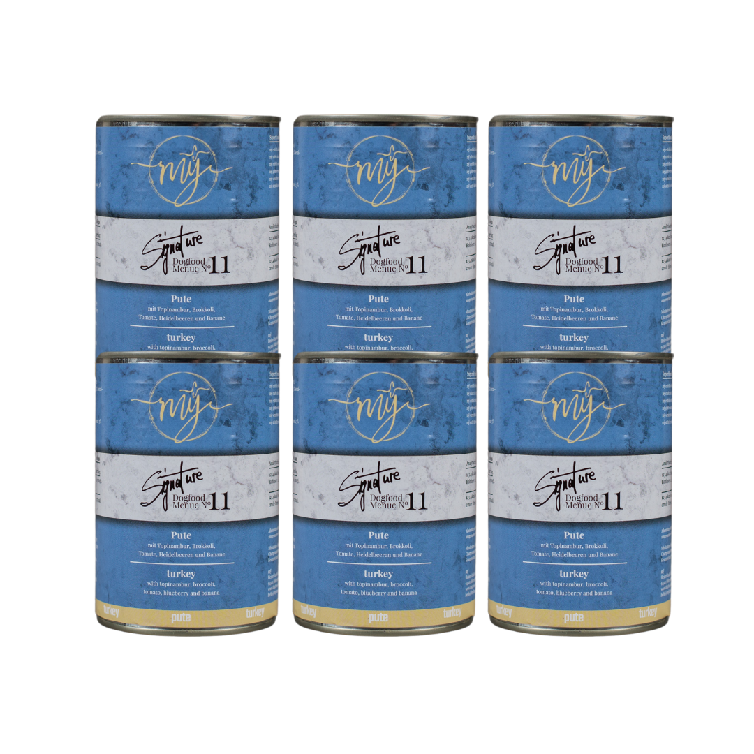 Sechs Dosen Hundefutter mit blauem Etikett. Aufschrift: my Signature, Dogfood Menue No. 11, BIO Pute und Zutaten wie Topinambur, Brokkoli, Heidelbeeren, Tomaten, Bananen,