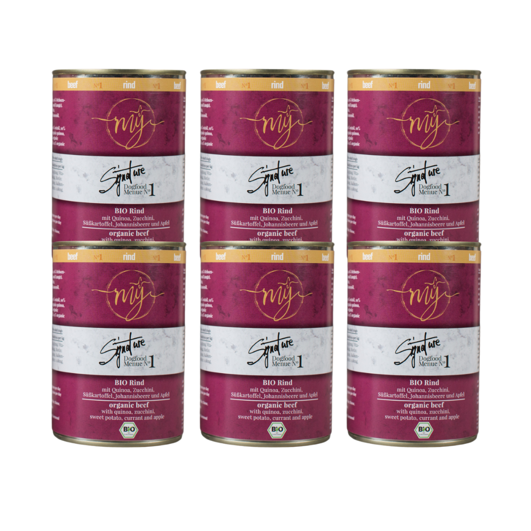 Sechs Dosen Hundefutter mit pinkem Etikett. Aufschrift: my Signature, Dogfood Menue No. 1, BIO Rins und Zutaten wie Quinoa, Zucchini, Süßkartoffeln, Johannsibeeren, Apfel