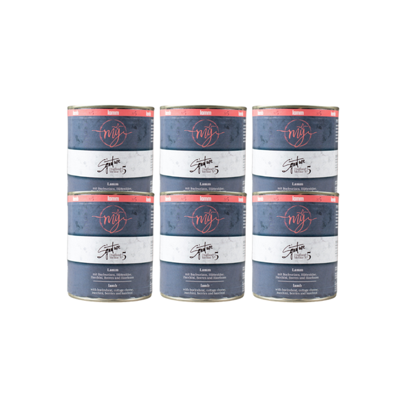 Sechs Dosen Hundefutter mit blauem Etikett. Aufschrift: my Signature, Dogfood Menue No.5, Lamm und Zutaten wie Buchweizen, Zucchini, Hüttenkäse, Cranberry, Heidelbeeren, Haselnuss