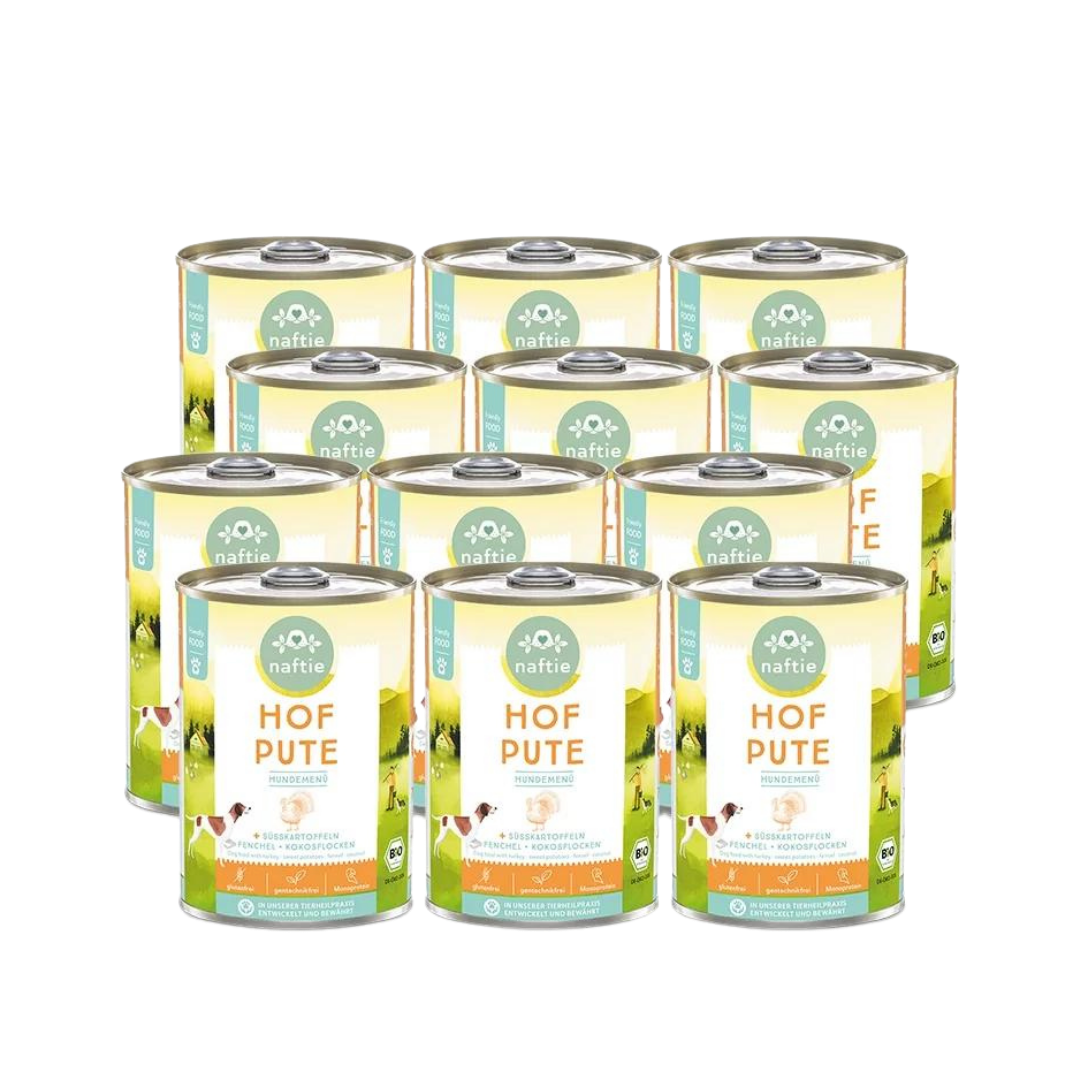 Zwölf Dosen mit Bio-Hundefutter von naftie, 400g, mit Abbildung eines Hundes und Landschaft im Hintergrund. Aufschrift: 'HOF PUTE HUNDEMENÜ.