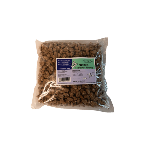 Transparente Verpackung mit 500 g Cookies von der Marke 'NEXT'. Die Cookies haben eine unregelmäßige Form und sind braun. Auf der Vorderseite befindet sich ein Etikett mit Produktinformationen.