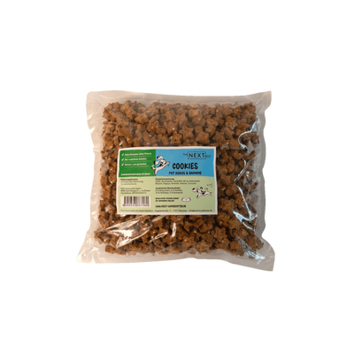 Transparente Verpackung mit 500 g Cookies von der Marke 'NEXT'. Die Cookies haben eine unregelmäßige Form und sind braun. Auf der Vorderseite befindet sich ein Etikett mit Produktinformationen.