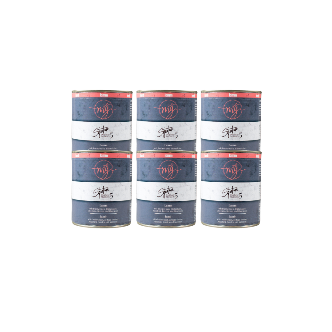 Sechs Dosen Hundefutter mit blauem Etikett. Aufschrift: my Signature, Dogfood Menue No.5, Lamm und Zutaten wie Buchweizen, Zucchini, Hüttenkäse, Cranberry, Heidelbeeren, Haselnuss