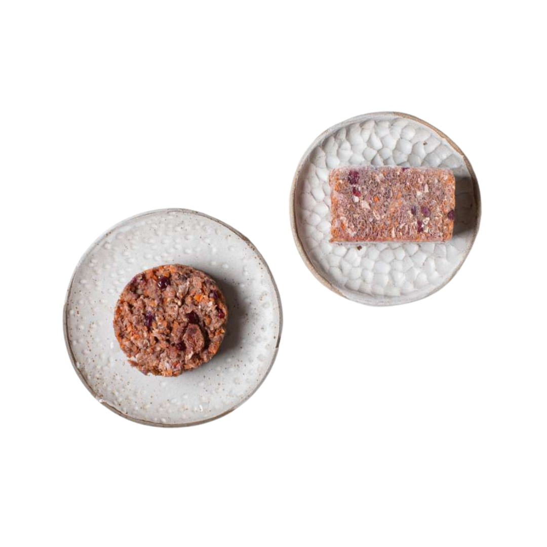 Zwei weiße Teller mit strukturiertem Muster, einer mit einem runden, der andere mit einem rechteckigen, braunen Lebensmittelstück mit sichtbaren Körnern und Nüssen.