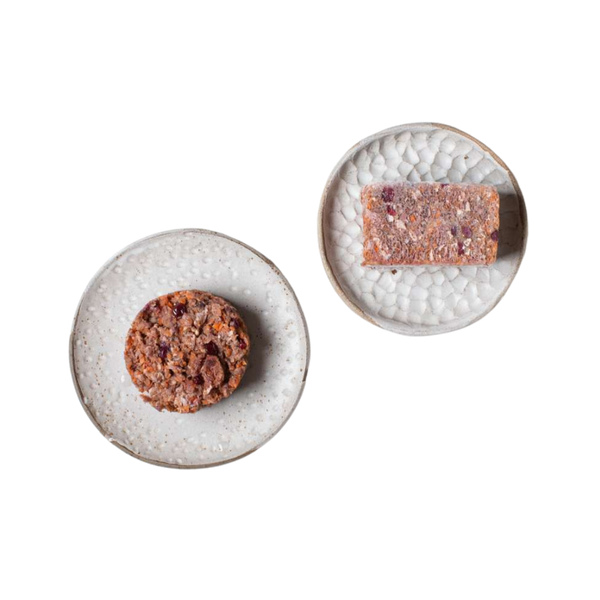 Zwei weiße Teller mit strukturiertem Muster, einer mit einem runden, der andere mit einem rechteckigen, braunen Lebensmittelstück mit sichtbaren Körnern und Nüssen.