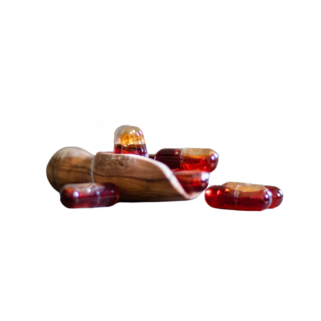 Mehrere rote Kapseln liegen auf und vorm einem Holzlöffel, eine Kapsel liegt daneben.