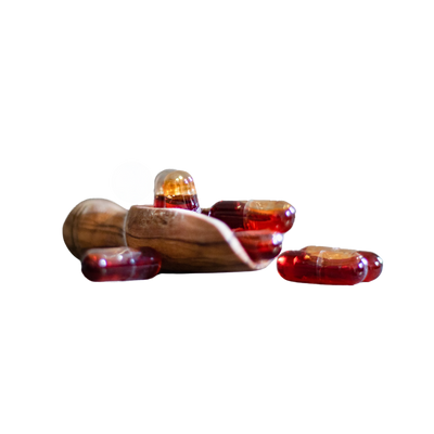 Mehrere rote Kapseln liegen auf und vorm einem Holzlöffel, eine Kapsel liegt daneben.