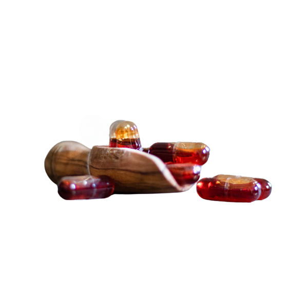 Mehrere rote Kapseln liegen auf und vorm einem Holzlöffel, eine Kapsel liegt daneben.