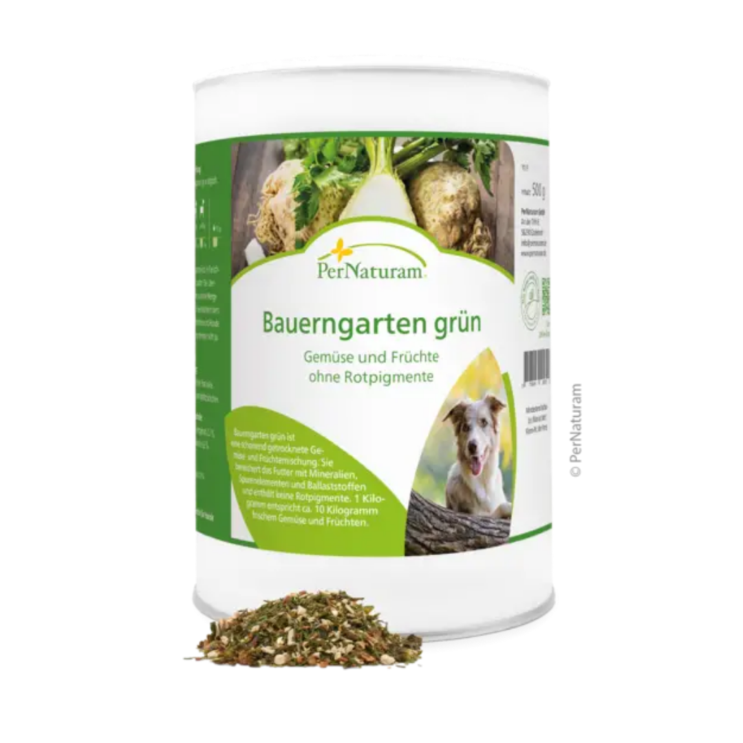Weißer Behälter mit grünem Etikett der Marke PerNaturam, Produktname 'Bauerngarten grün', mit Text "Gemüse und Früchte ohne Rotpigmente" und einem Bild eines braun und weißen Hundes, davor lose Kräutermischung.