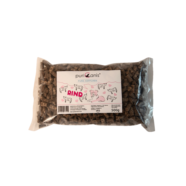 PuriCanis Pure Häppchen Rind, 500g Packung mit braunen, rechteckigen Hundeleckerlis, auf der Verpackung Zeichnungen von Rindern und einem Hund.