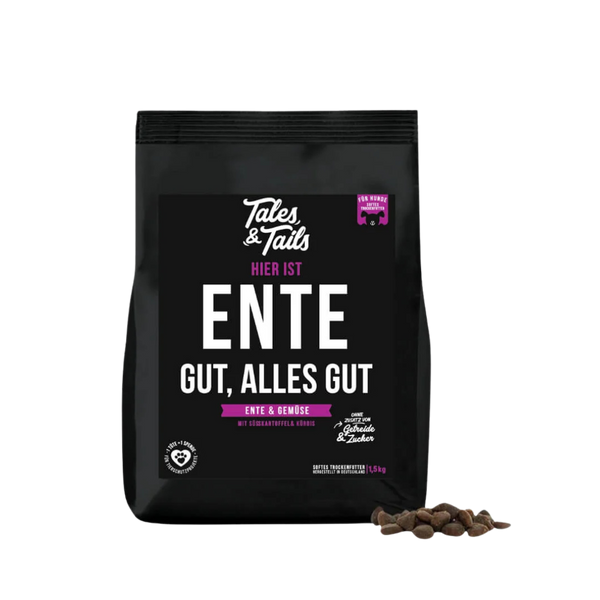 Schwarze Verpackung von Tales & Tails halbfeuchtem Trockenfutter mit der Aufschrift 'Hier ist Ente gut, alles gut', daneben einige braune Futterstücke.