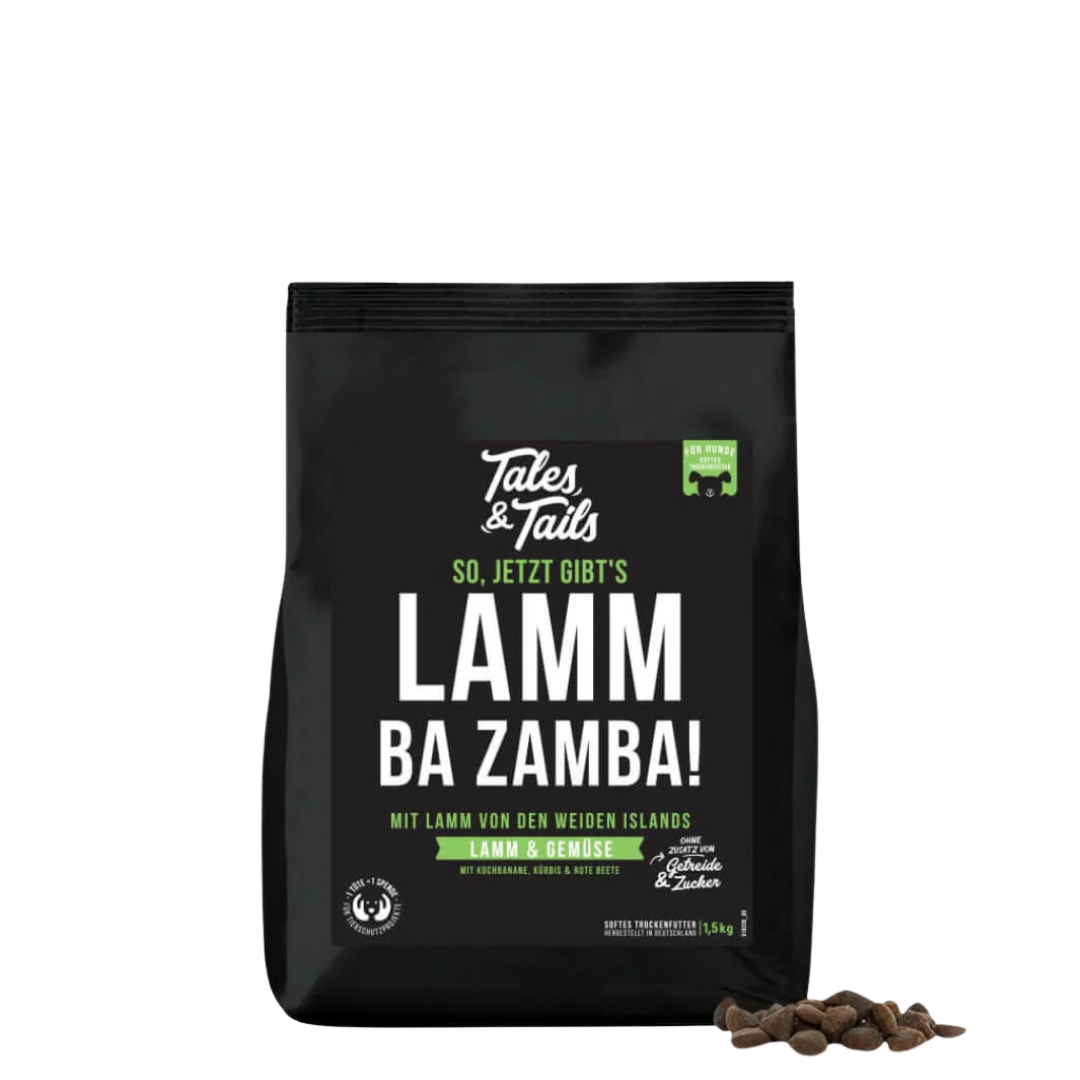 Schwarze Verpackung von Tales & Tails halbfeuchtem Trockenfutter mit der Aufschrift 'So, jetzt gibt s lamm ba zamba', daneben einige braune Futterstücke.