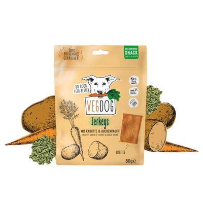 Beige Verpackung von Vegdog Jerkeys mit Hundekopf-Logo, Text 'Mit Karotte & Buchenrauch', Abbildung von Karotten und Kartoffeln, 80 Gramm.
