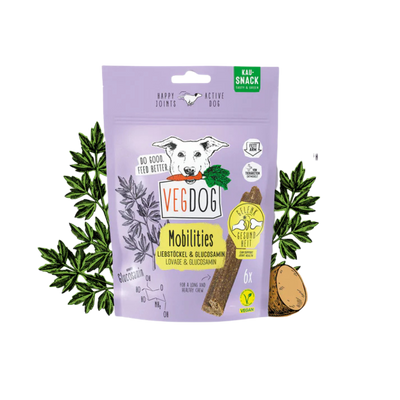 Lila Verpackung von Vegdog Mobilities Kausnack mit Hundekopf-Illustration, Text 'Liebestöckel & Glucosamin', sechs vegane Snacks, umgeben von Pflanzen und Kartoffeln.