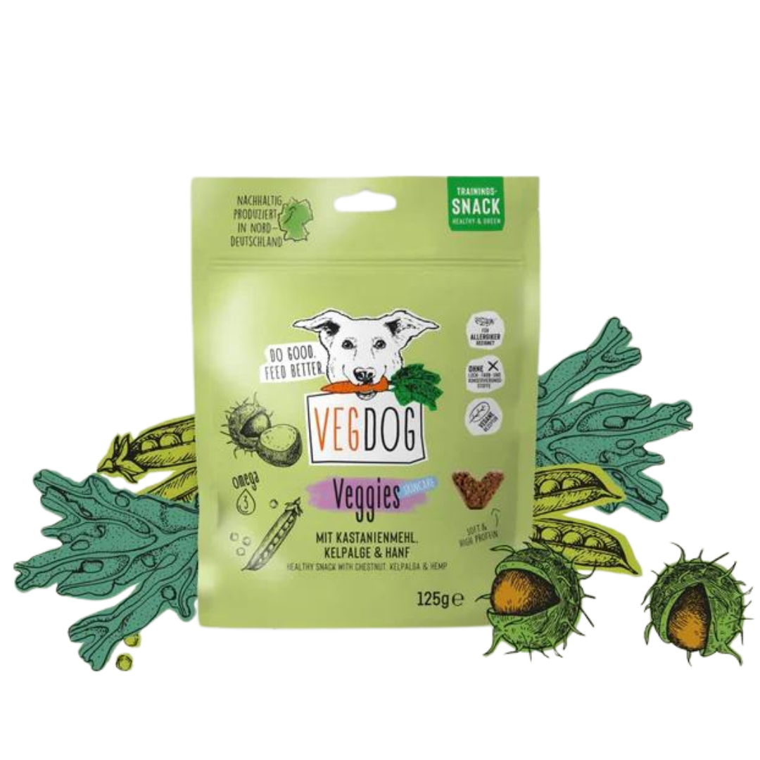 Grüne Verpackung mit der Aufschrift 'VEGDOG Veggies Snack', Bild eines weißen Hundes mit Karotte im Maul, umgeben von Illustrationen von Kastanien und grünen Blättern.